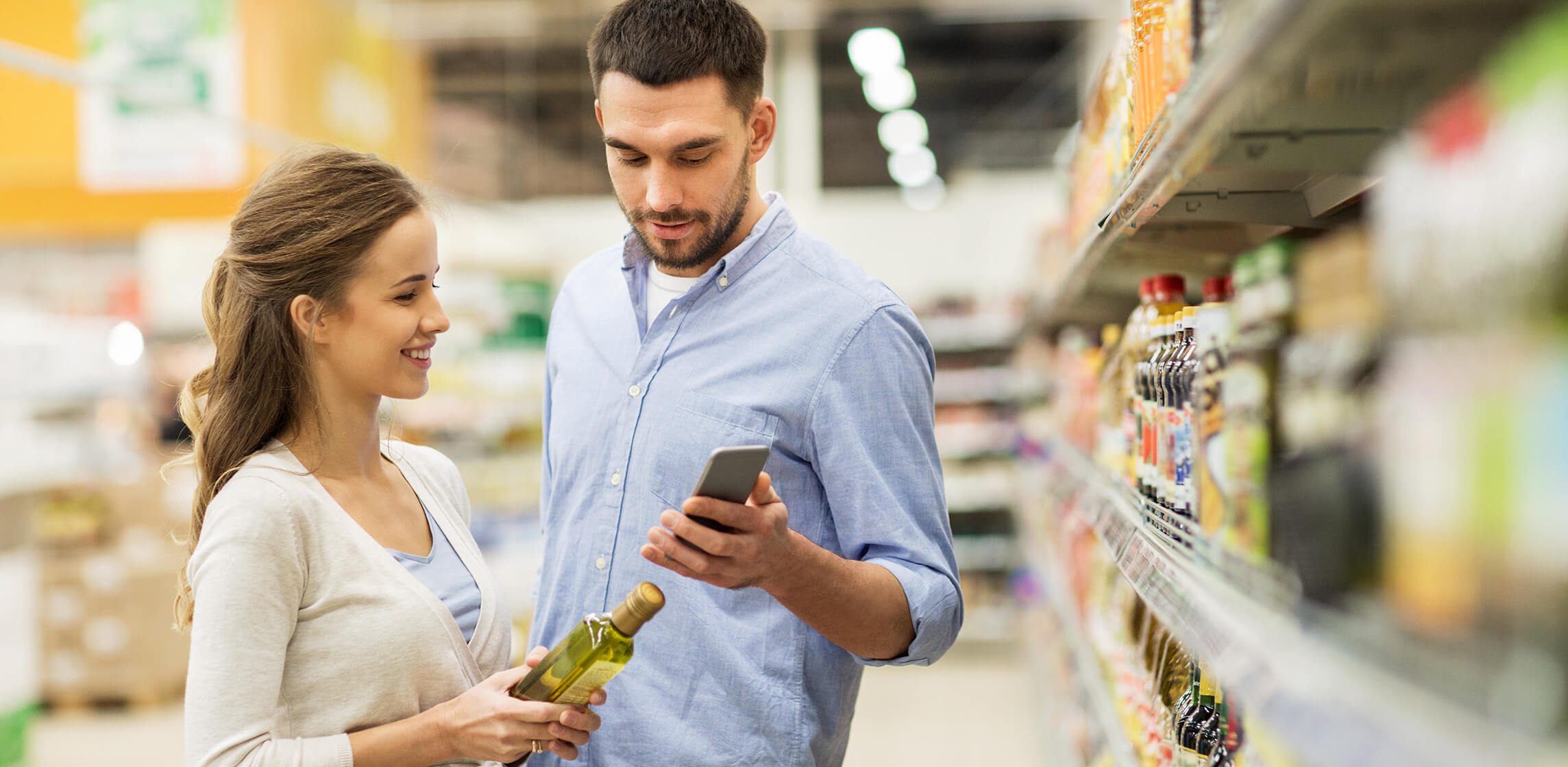Couple checking a bottle of oil against a smartphone app while grocery shopping