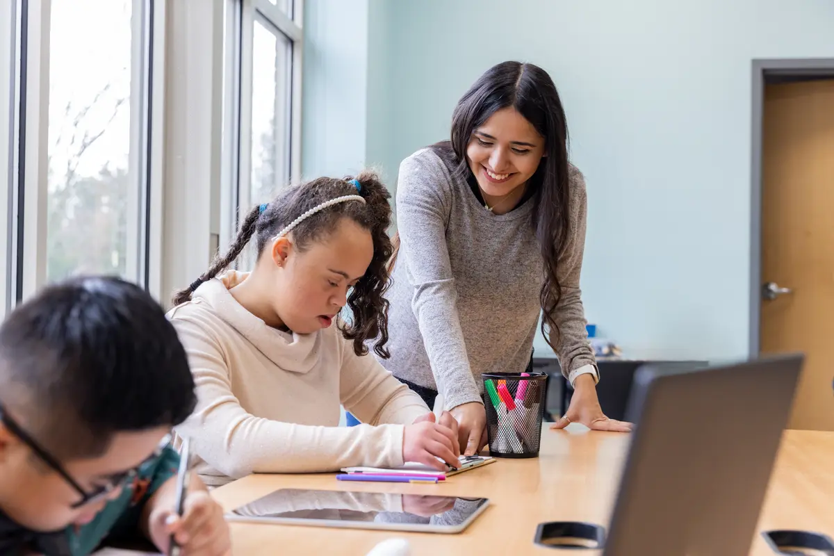 Special education teacher helping a student with Down syndrome with a writing activity in class