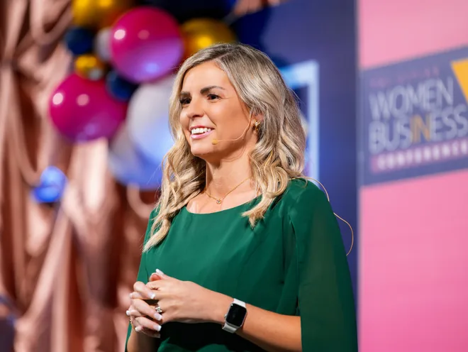 Missy Moss Wright speaking in front of a Women in Business Conference backdrop