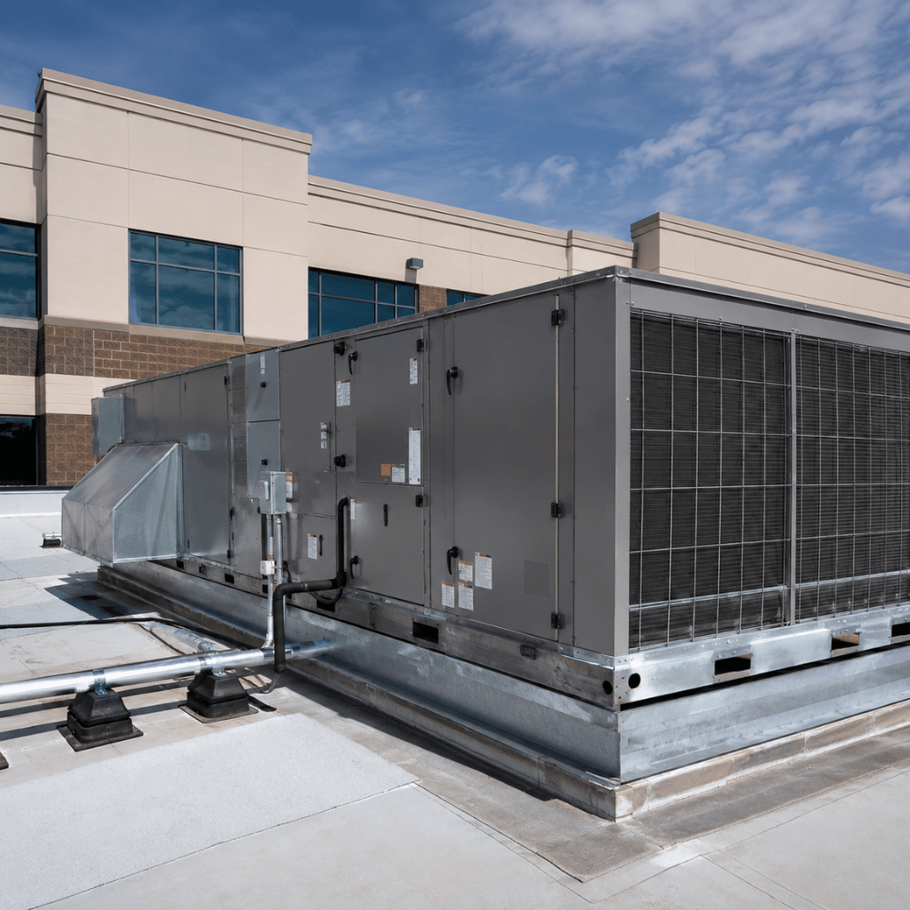 Large commercial HVAC unit on a rooftop next to a beige and brown building under a blue sky.