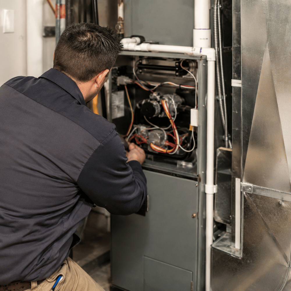 Technician in navy uniform repairing the inside of a furnace with tools in a basement.