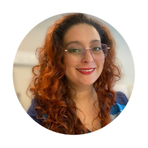 Retrato de Fernanda, cabello rizado colorín y gafas, sonriendo con labial rojo y fondo desenfocado.