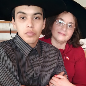 Retrato de Nora y su hijo. Mujer mayor y niño preadolescente, ambos con sombreros, mujer con gafas y camiseta roja, posando juntos.