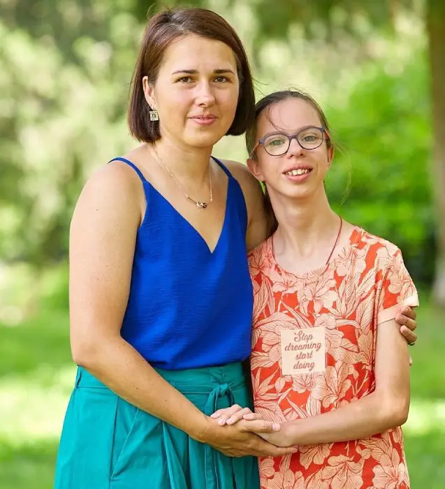 Dos mujeres abrazándose en un parque, una lleva blusa azul y la otra camiseta naranja con flores.