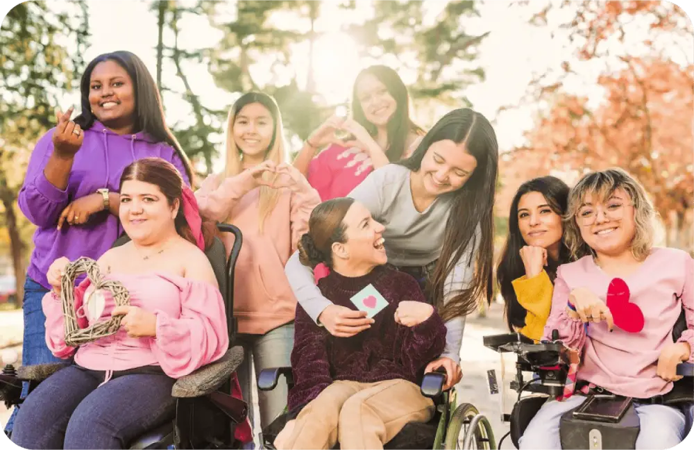 Grupo diverso de mujeres sonrientes, algunas en sillas de ruedas, mostrando corazones con las manos.