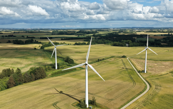 Three large wind turbines in green fields under a partly cloudy sky.