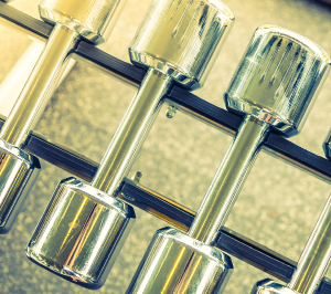 Shiny silver dumbbells arranged on a black metal rack in a gym setting.
