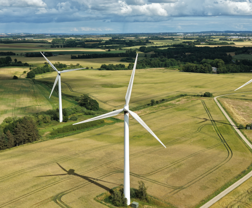 Aerial view of wind turbines on green farmland under a cloudy sky.