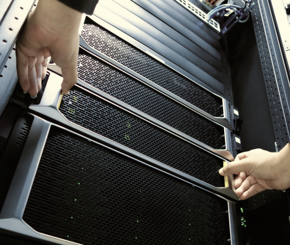 Hands installing or removing a server unit in a black server rack with green indicator lights.