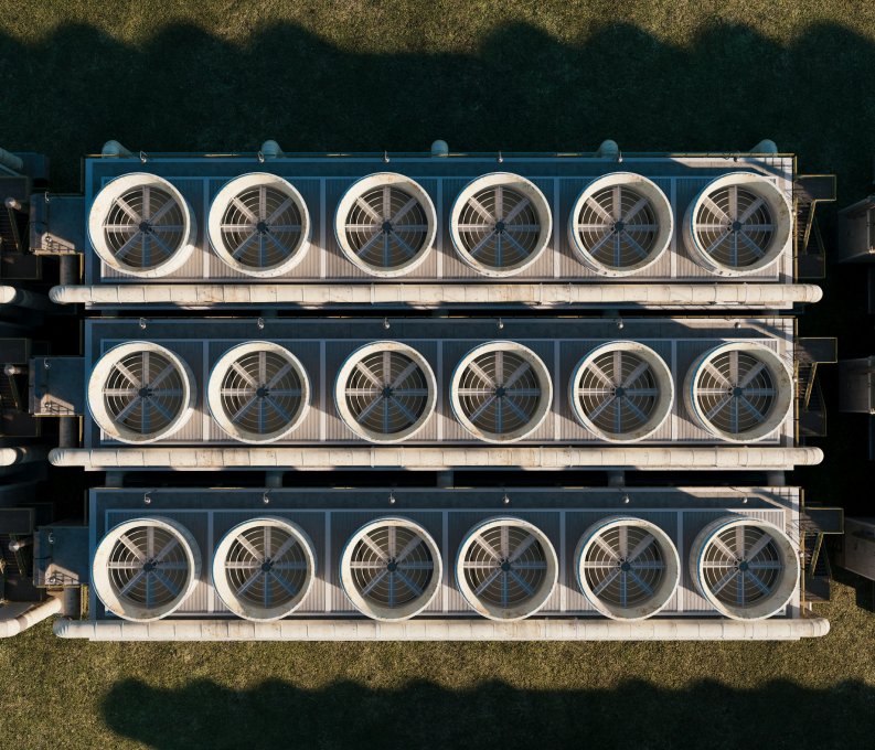 Aerial view of three rows of large industrial cooling fans with grass and shadows around.