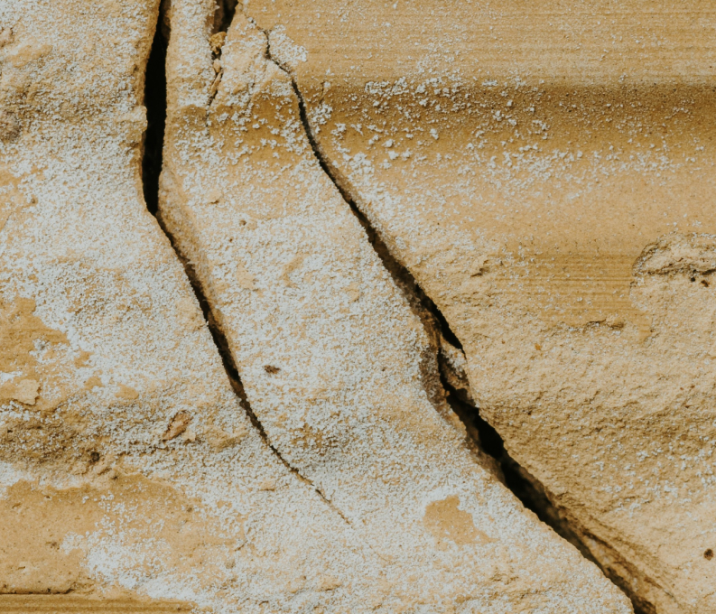 Close-up of cracked, sandy-textured light brown surface with rough patches.