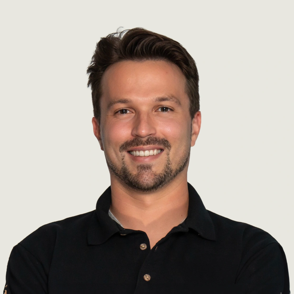 Smiling man with short brown hair and trimmed beard wearing a black collared shirt.