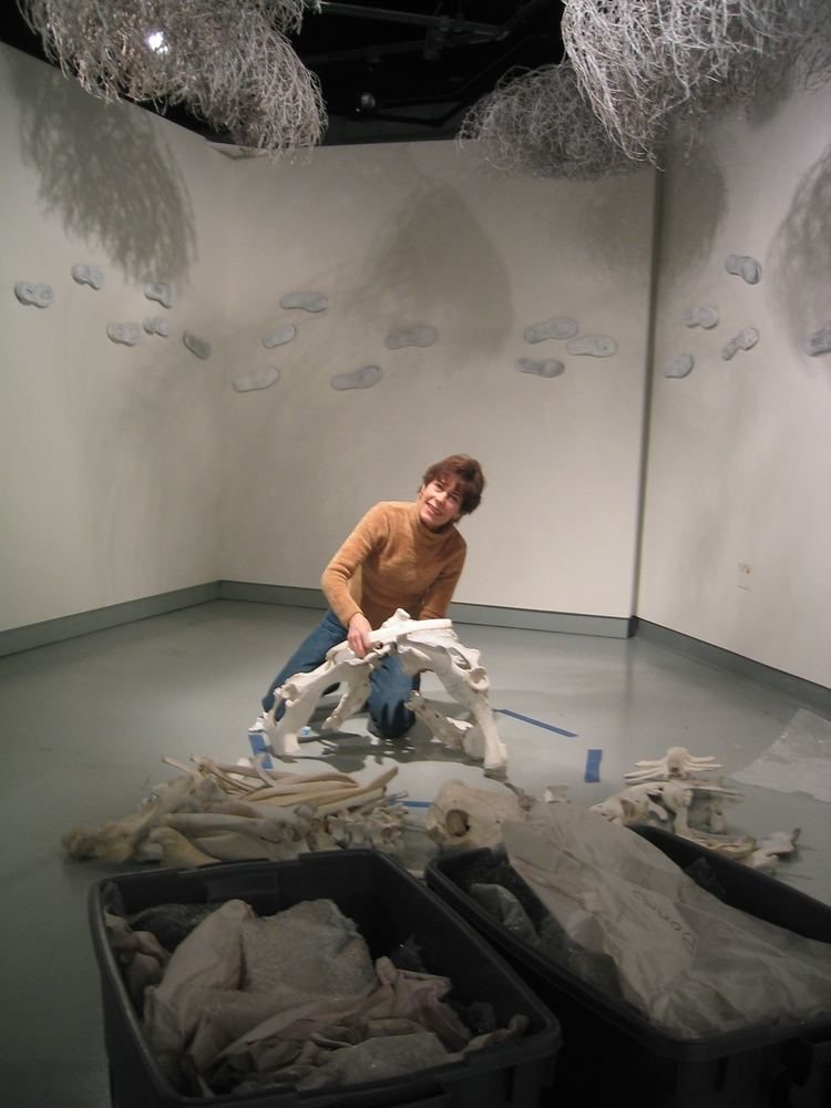 At the Crossroads during installation, the artist crouched in the gallery corner working on a floor piece with wire forms suspended above