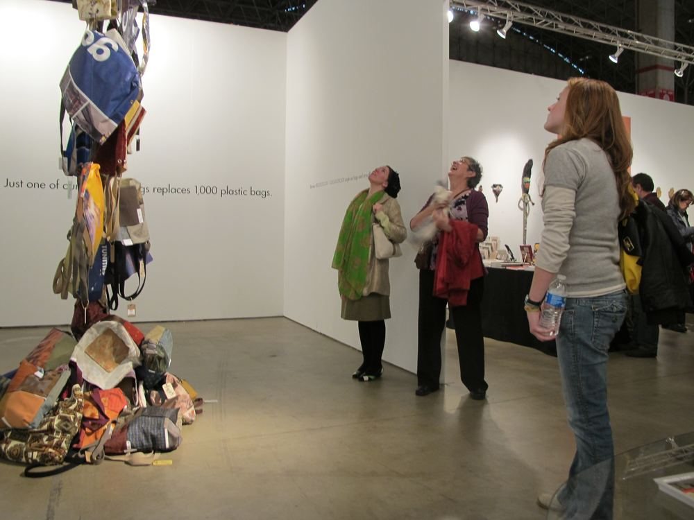 Bags Across the Globe at SOFA Chicago, two visitors beside a tall hanging column of handmade bags and a pile of bags on the floor