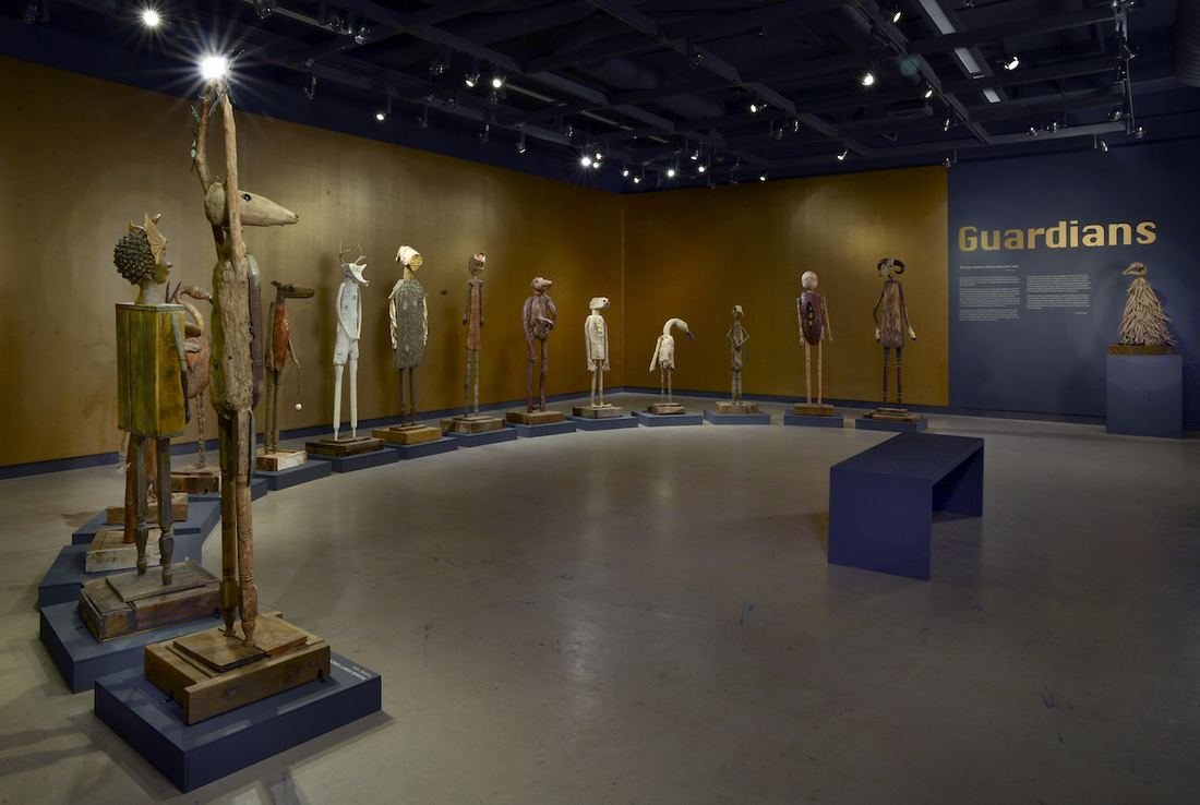 Guardians: Spirits of Protection at the Morris Graves Museum of Art, a curved row of tall driftwood figures standing on the gallery's wood floor