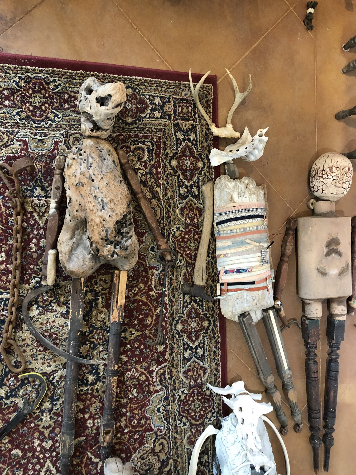 Part-built figures and loose driftwood parts propped against a patterned rug, with antlers among them