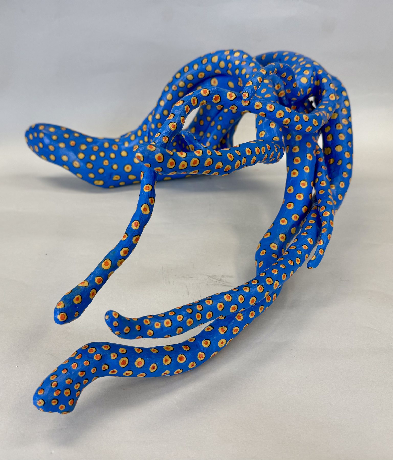 Hexapus, a many-armed driftwood form painted deep blue and spotted with gold, arms spreading outward