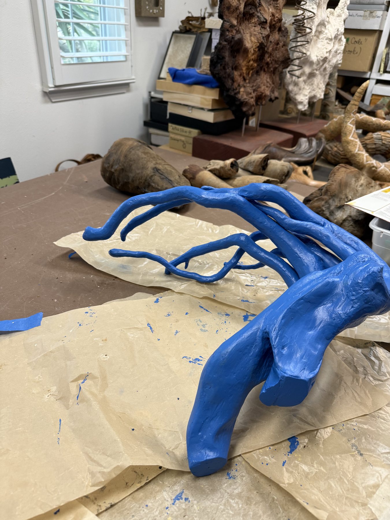 A driftwood piece half painted blue, resting on a drop cloth in the studio mid-process