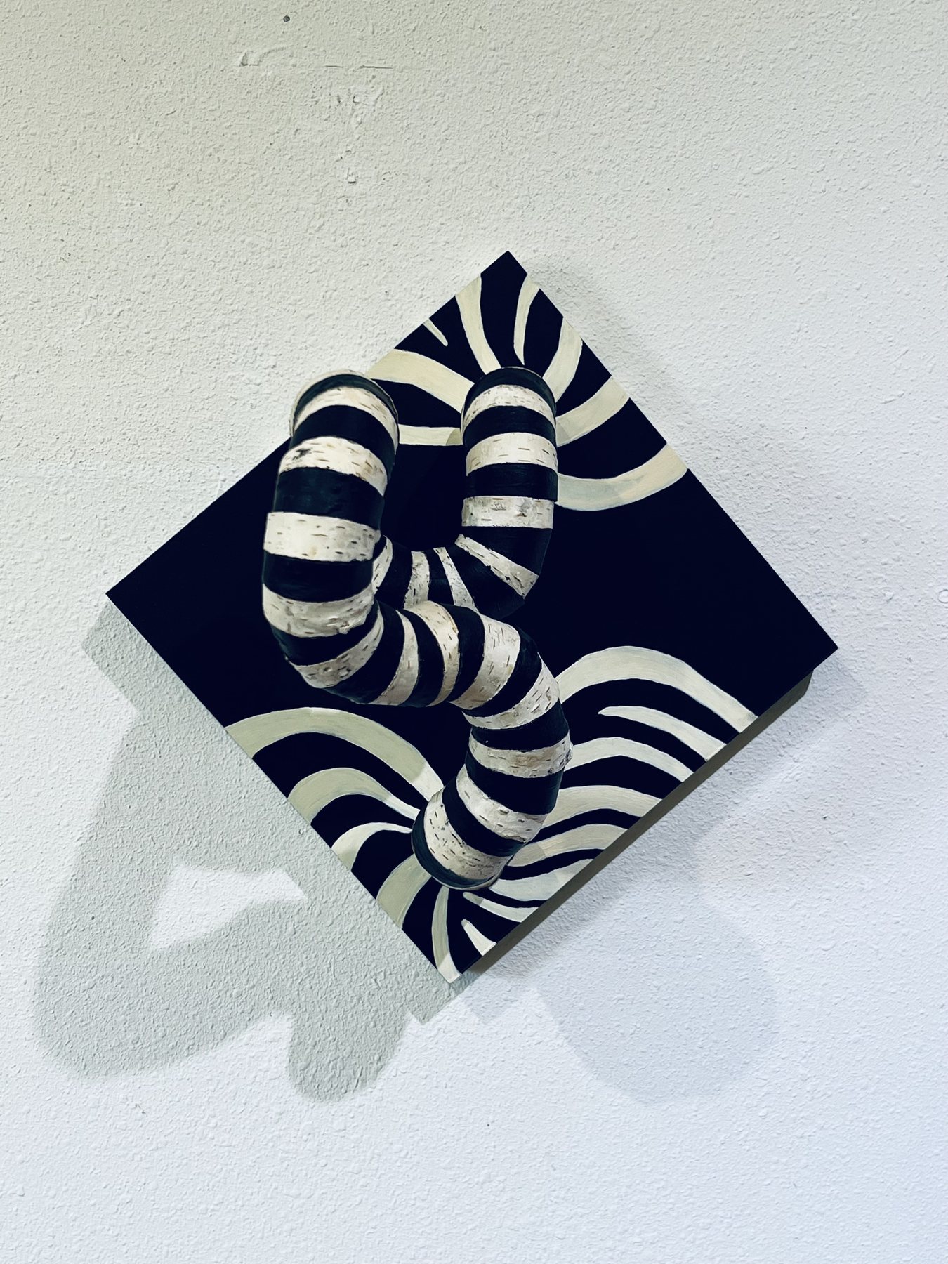 Zebra, second view: black and white striped wood on a navy diamond panel, hung on a white wall with a strong shadow