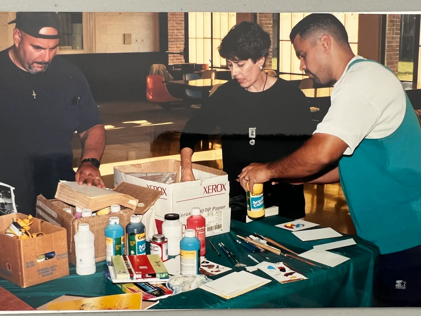 Ann Savageau at a table of art supplies with two men from the workshop