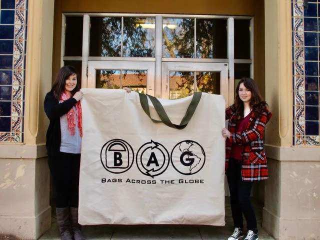 Two participants holding an oversized bag printed with the Bags Across the Globe logo