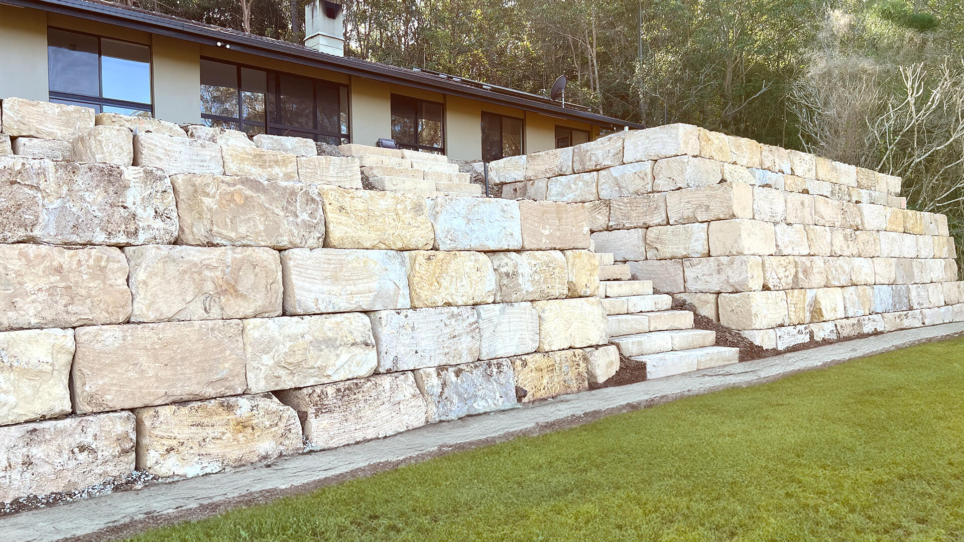 Terraced retaining wall made of large rectangular stone blocks with stairs leading to a building.