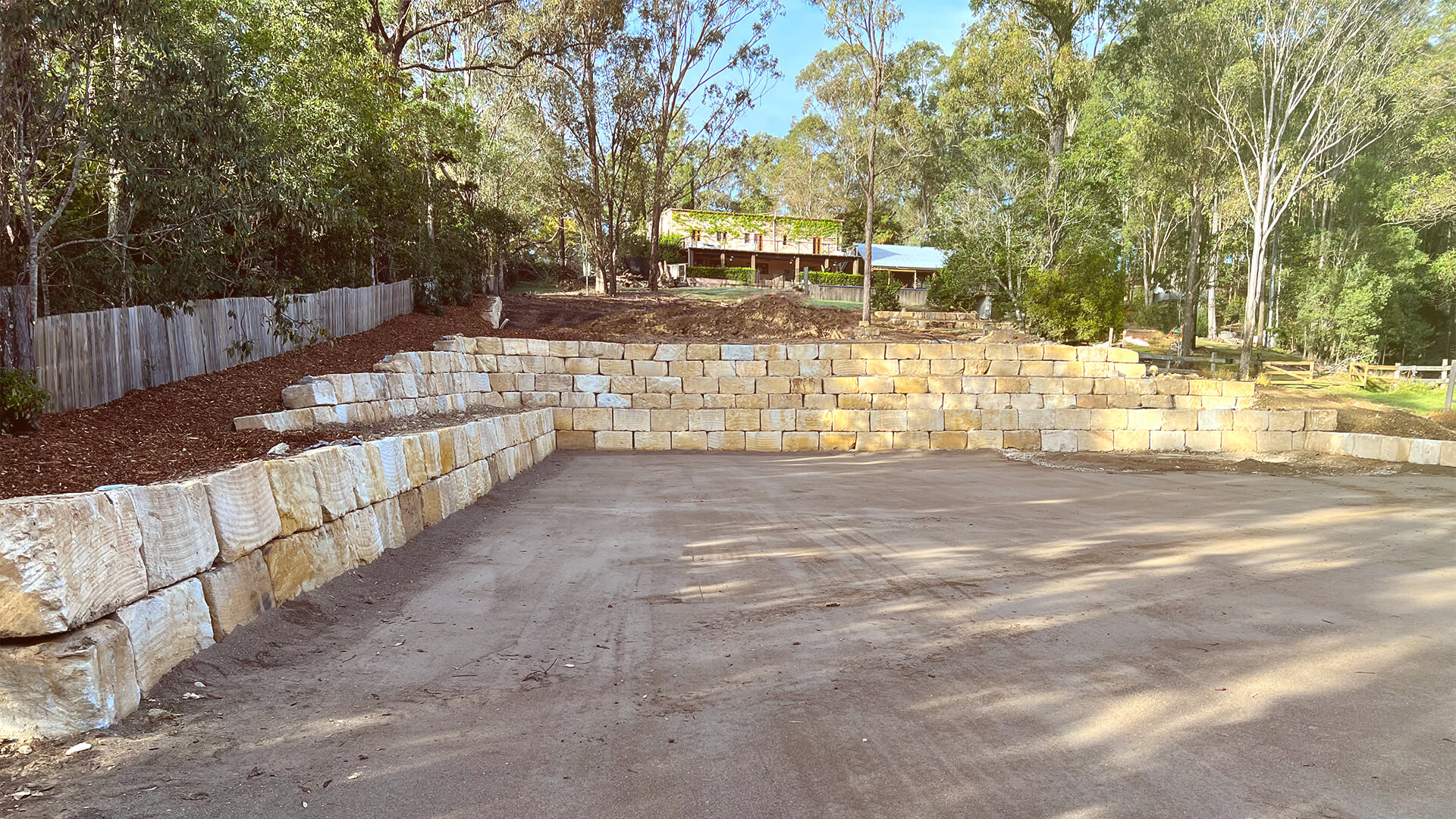 Terraced backyard with large stacked sandstone retaining walls and cleared area in front under trees.