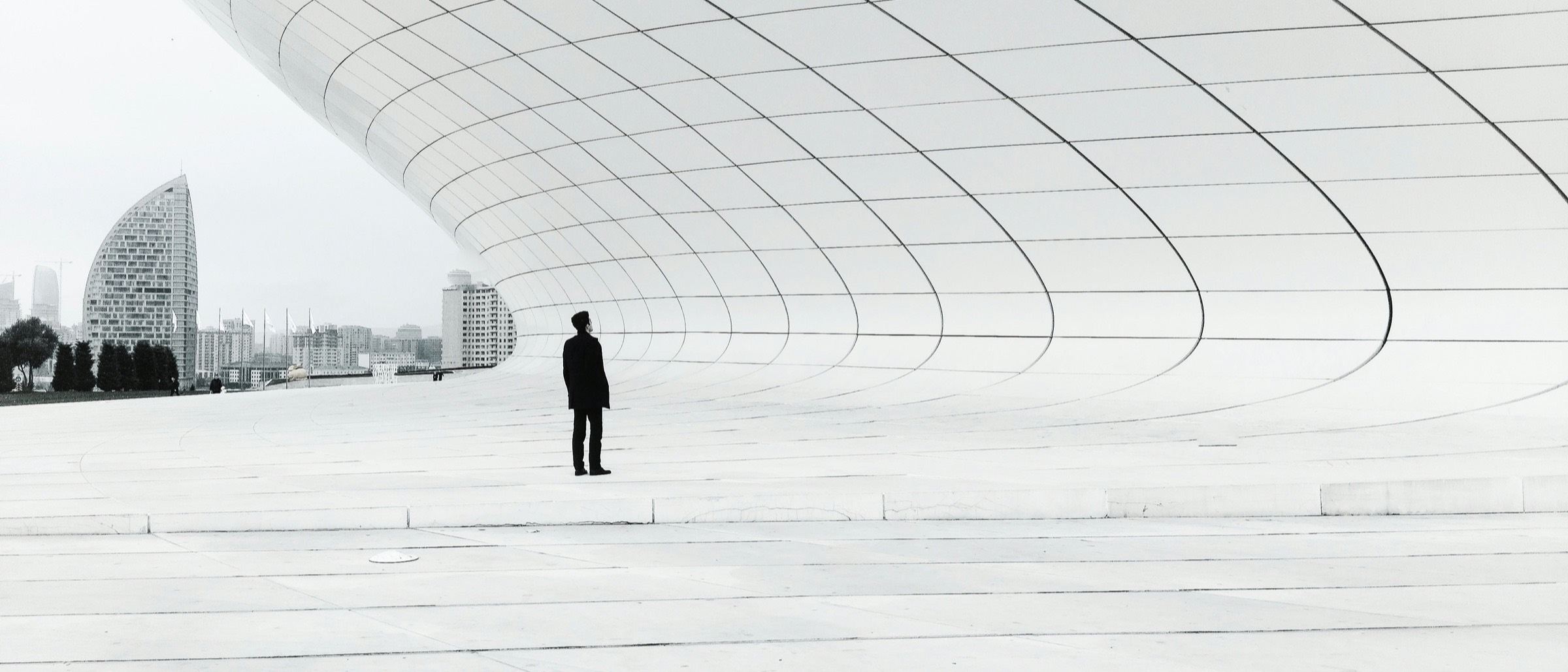 A lone figure standing in a vast, empty modernist plaza.