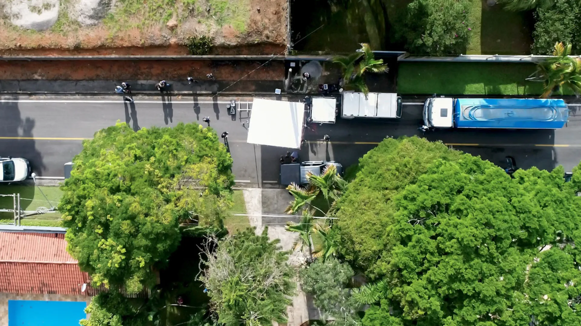 Vista aérea de um set de filmagem na rua, com caminhões, rebatedores e equipe