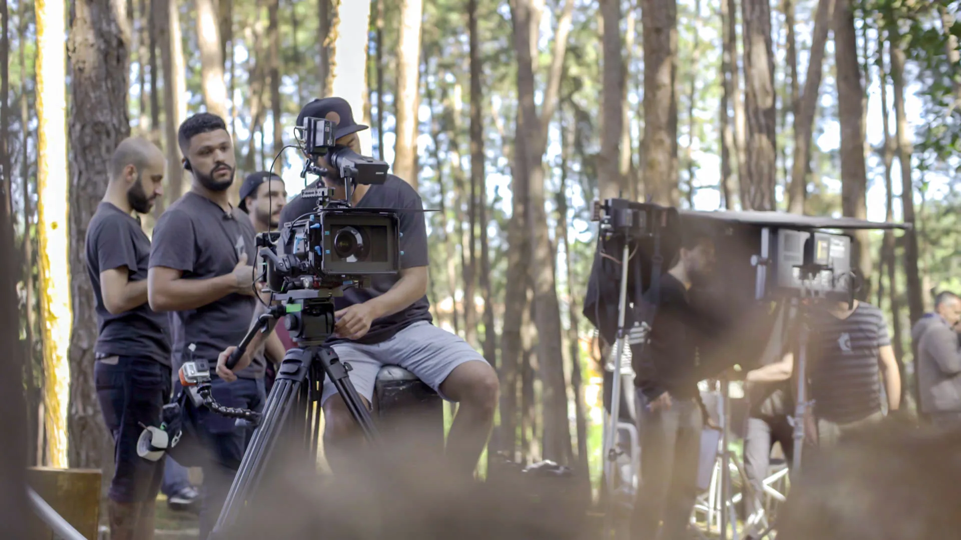 Equipe com câmera de cinema em tripé durante filmagem num bosque