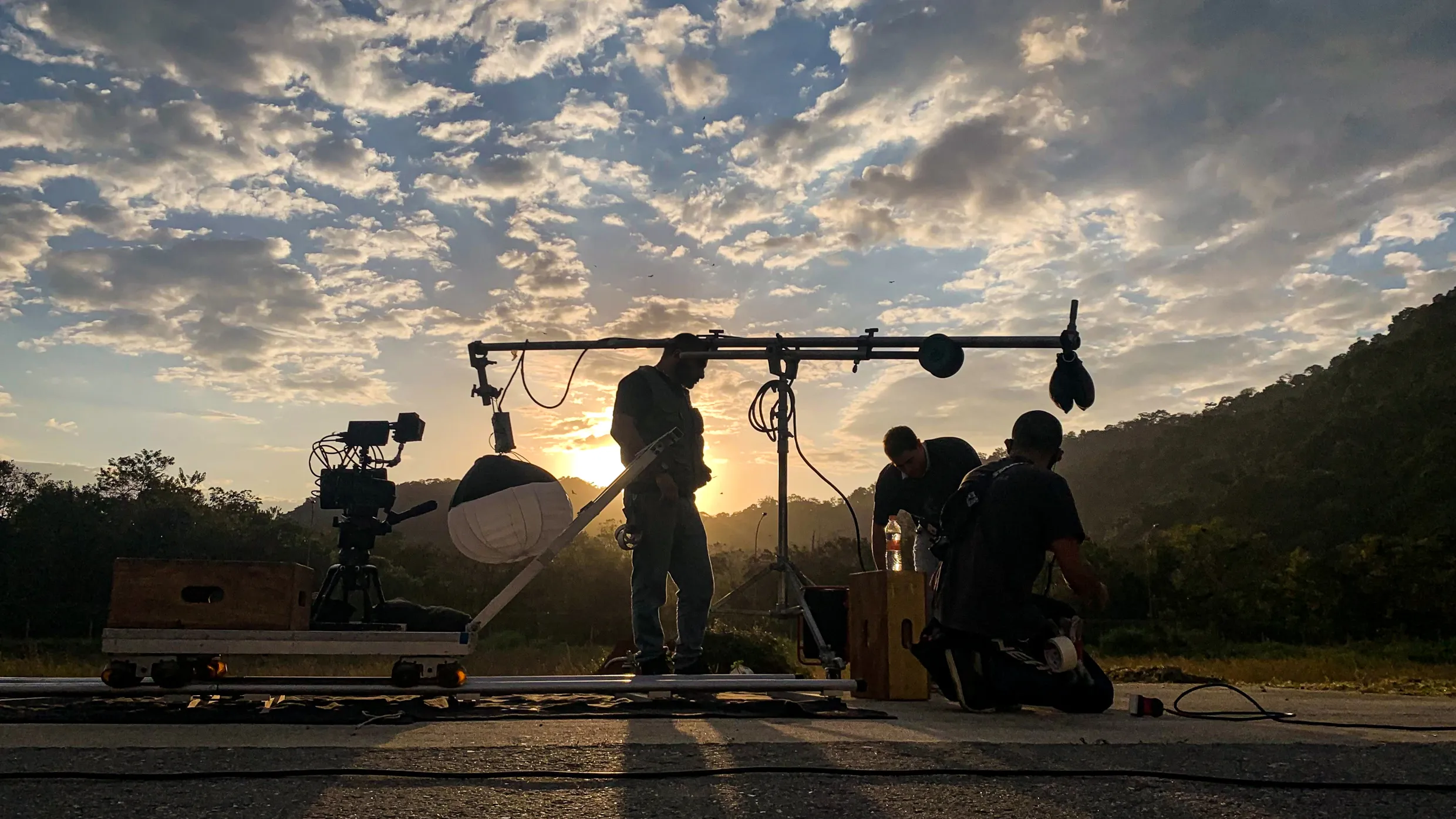 Equipe montando câmera, travelling e iluminação em set externo ao pôr do sol