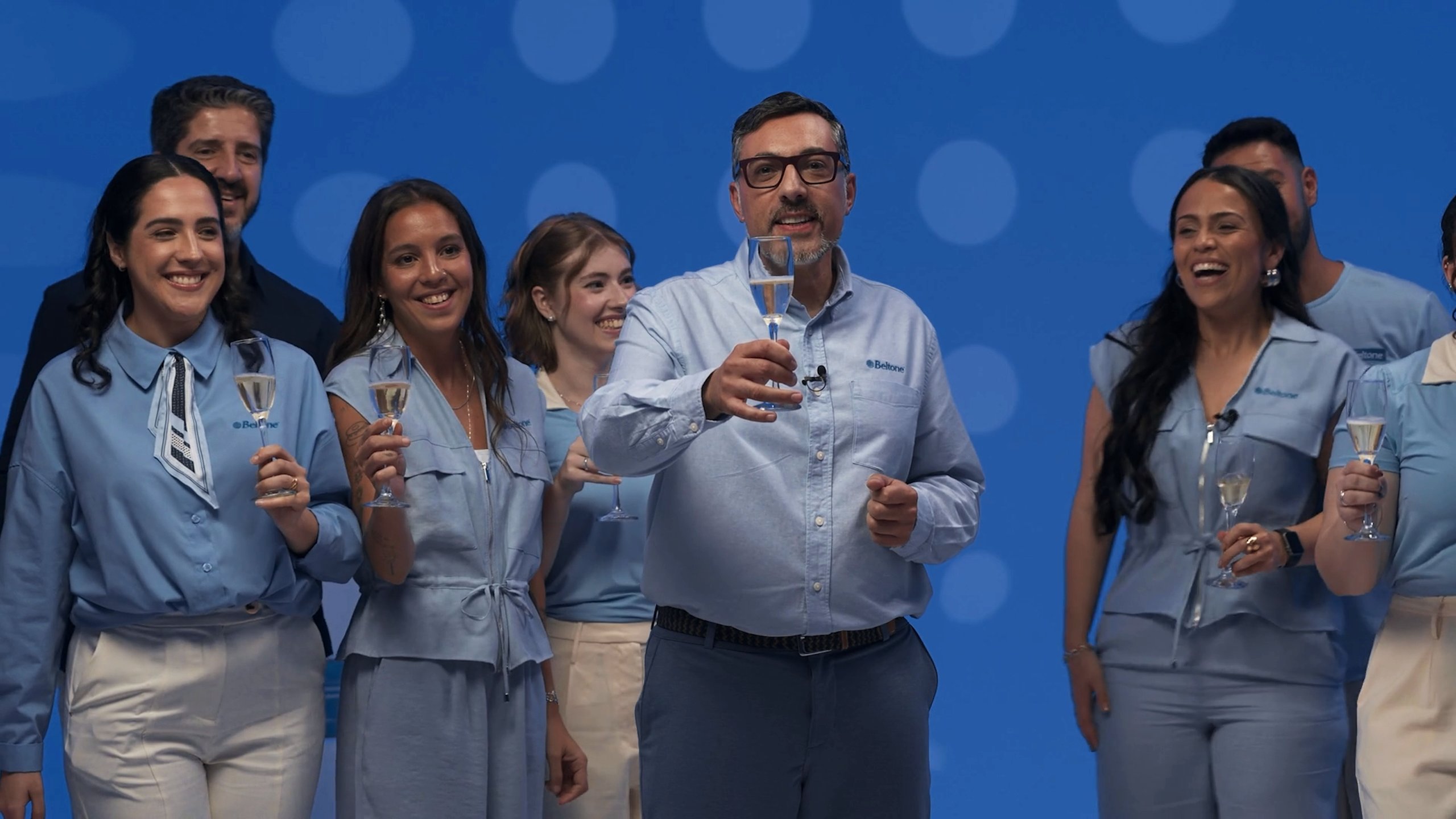 Elenco do programa brinda com taças no palco azul, rindo