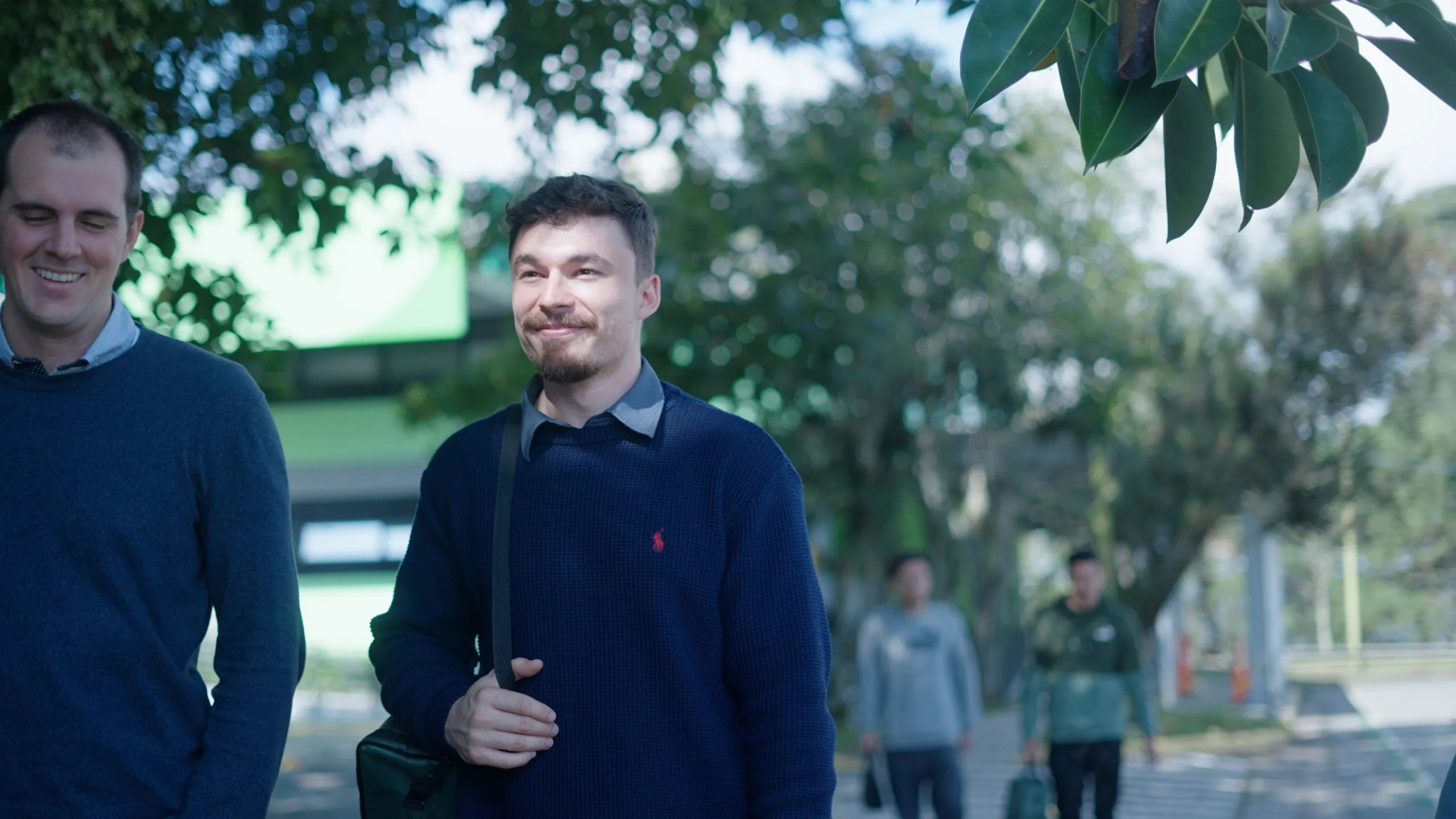 Dois homens caminham sorrindo por uma rua arborizada