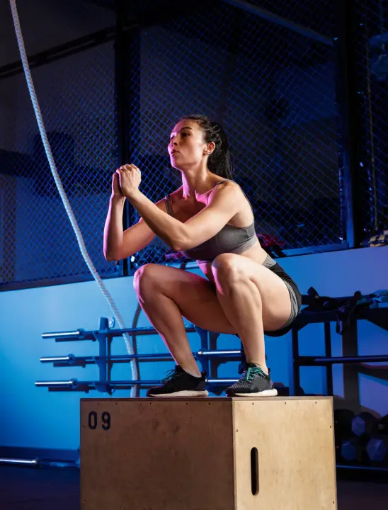 Woman performing a squat exercise on a plyometric box in a gym