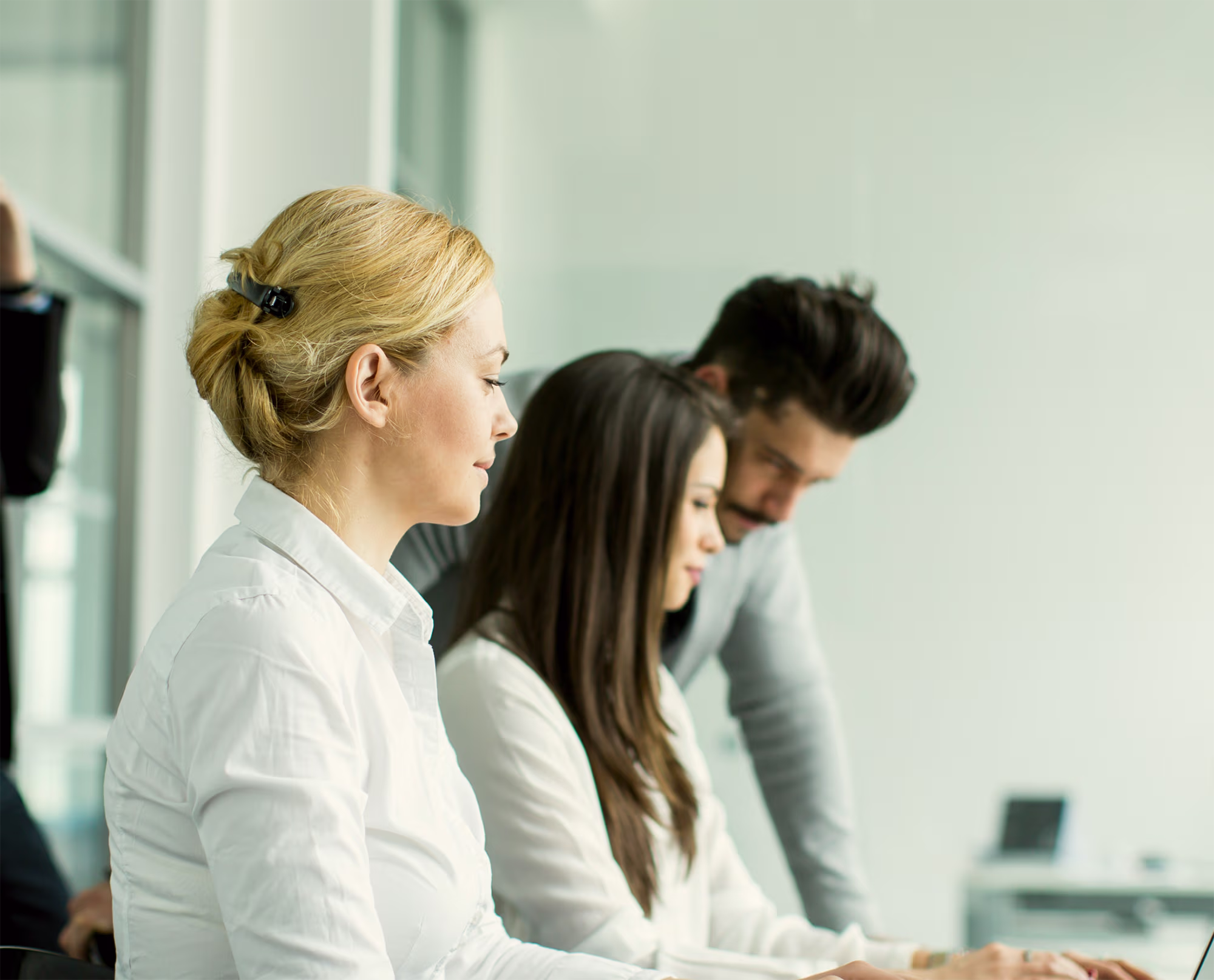 Three people working together in an office setting, two women and one man focused on a task at a desk.