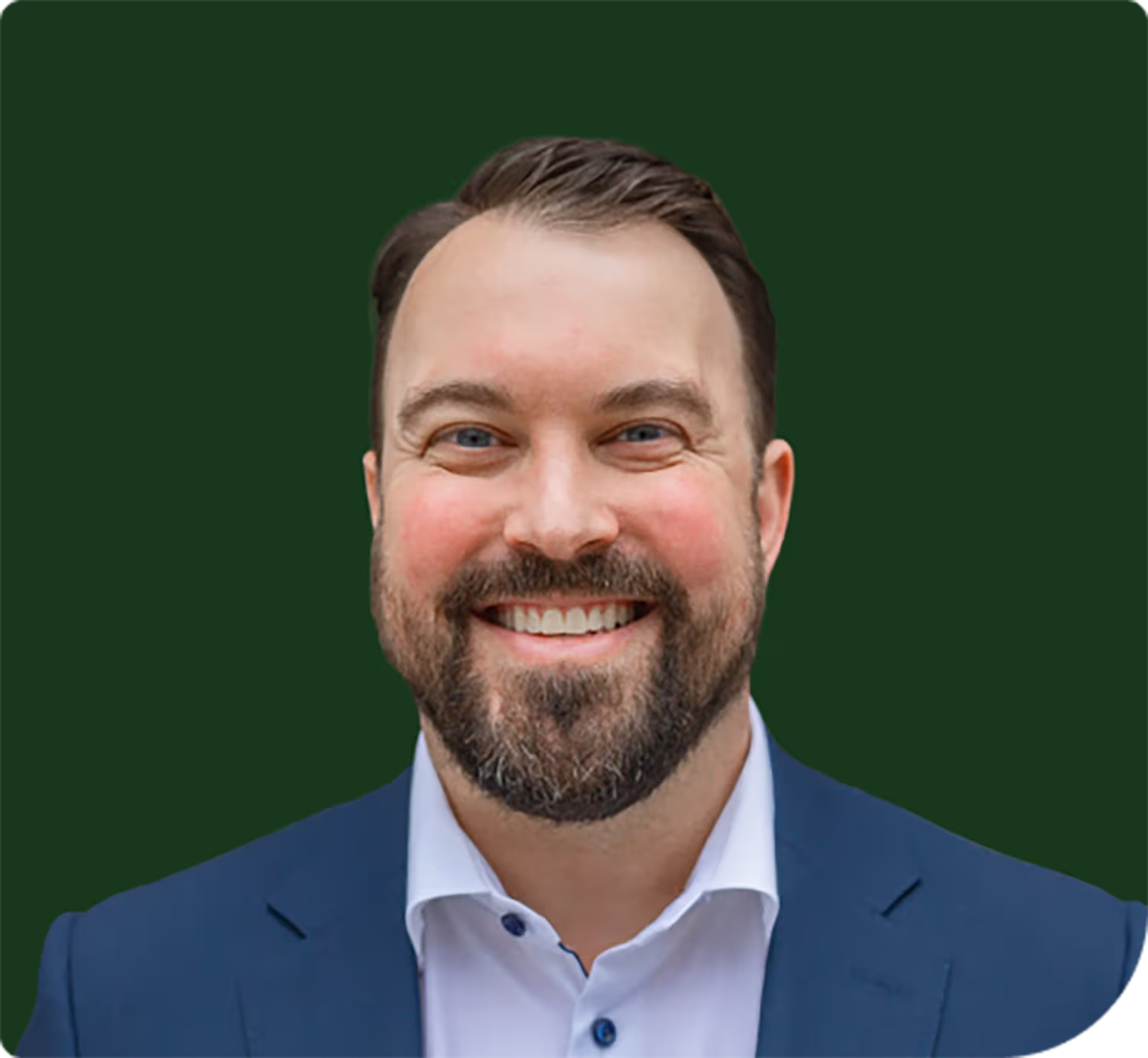 Smiling man with brown hair and beard wearing a blue suit jacket and white shirt against a dark green background.