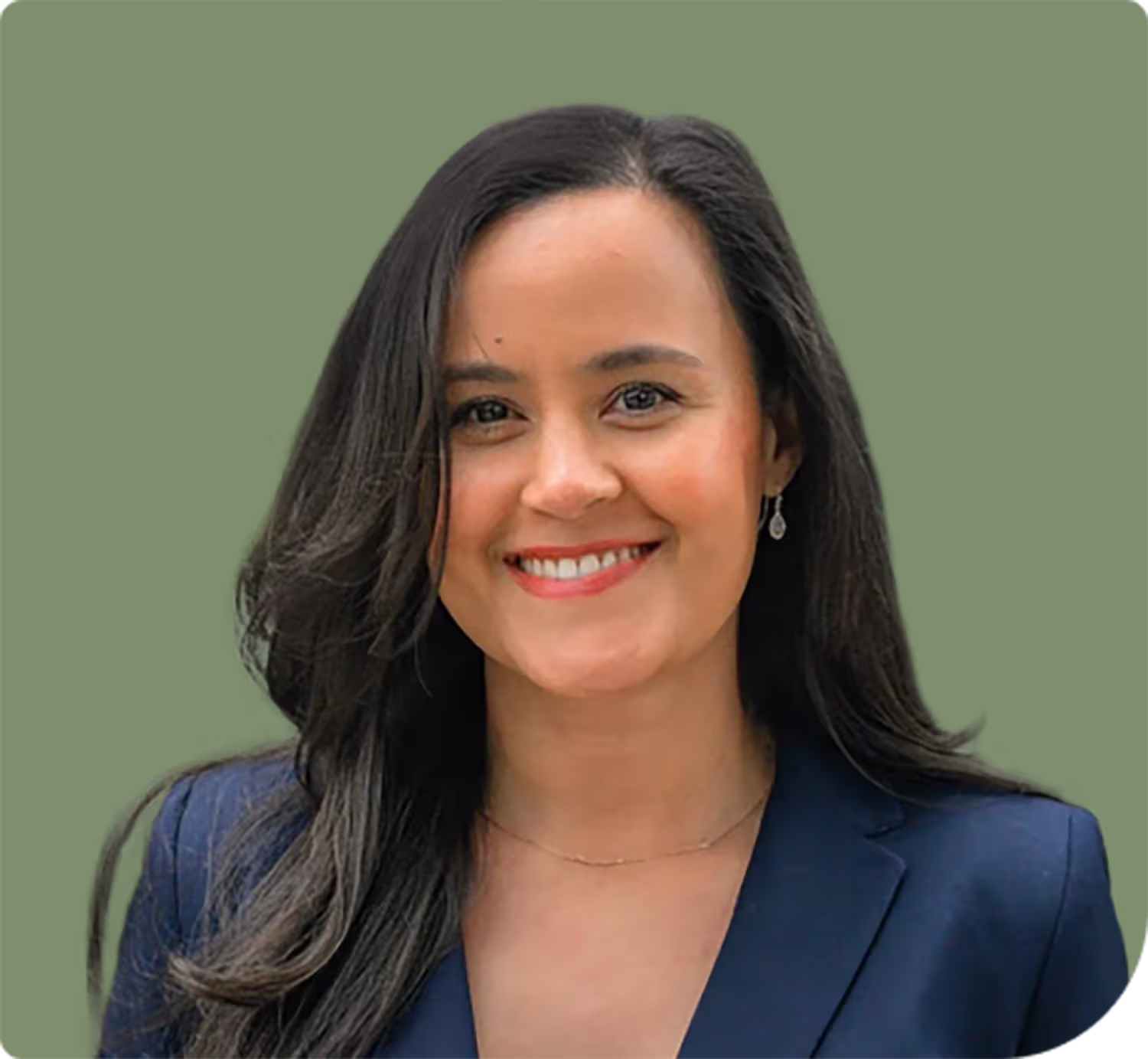 Smiling woman with long dark hair wearing a navy blazer and dangling earrings against a muted green background.