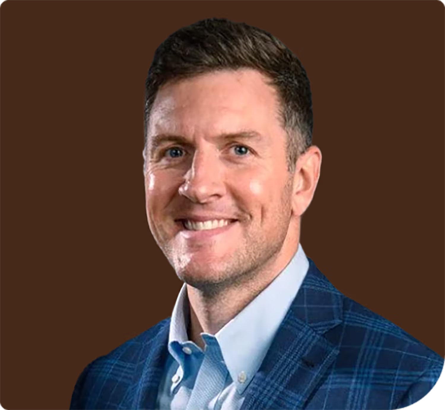Smiling man with short brown hair wearing a blue plaid suit jacket and light blue collared shirt against a brown background.