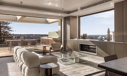 Modern living room with glass coffee table, fireplace, and floor-to-ceiling windows overlooking city and ocean.