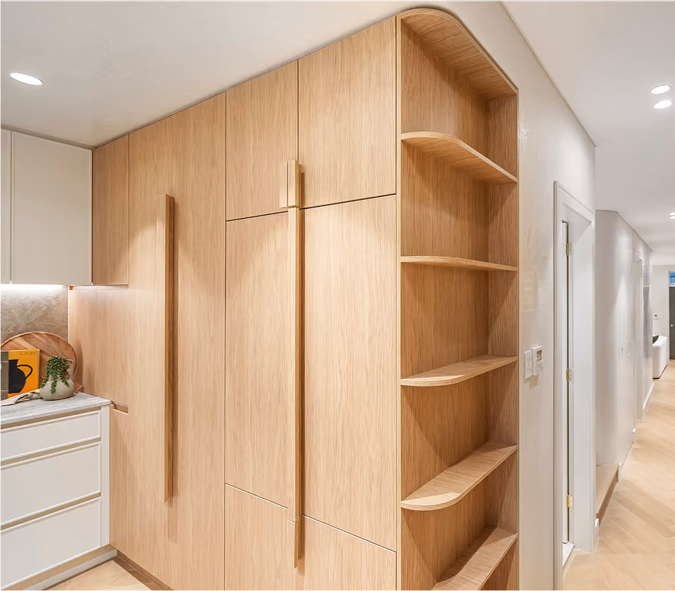 Modern kitchen corner with light wood cabinets and open curved wood shelves beside a hallway.