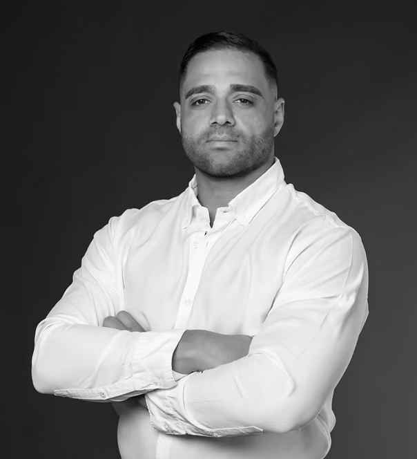 Black and white photo of a man with short hair in a white shirt with arms crossed, looking at the camera.
