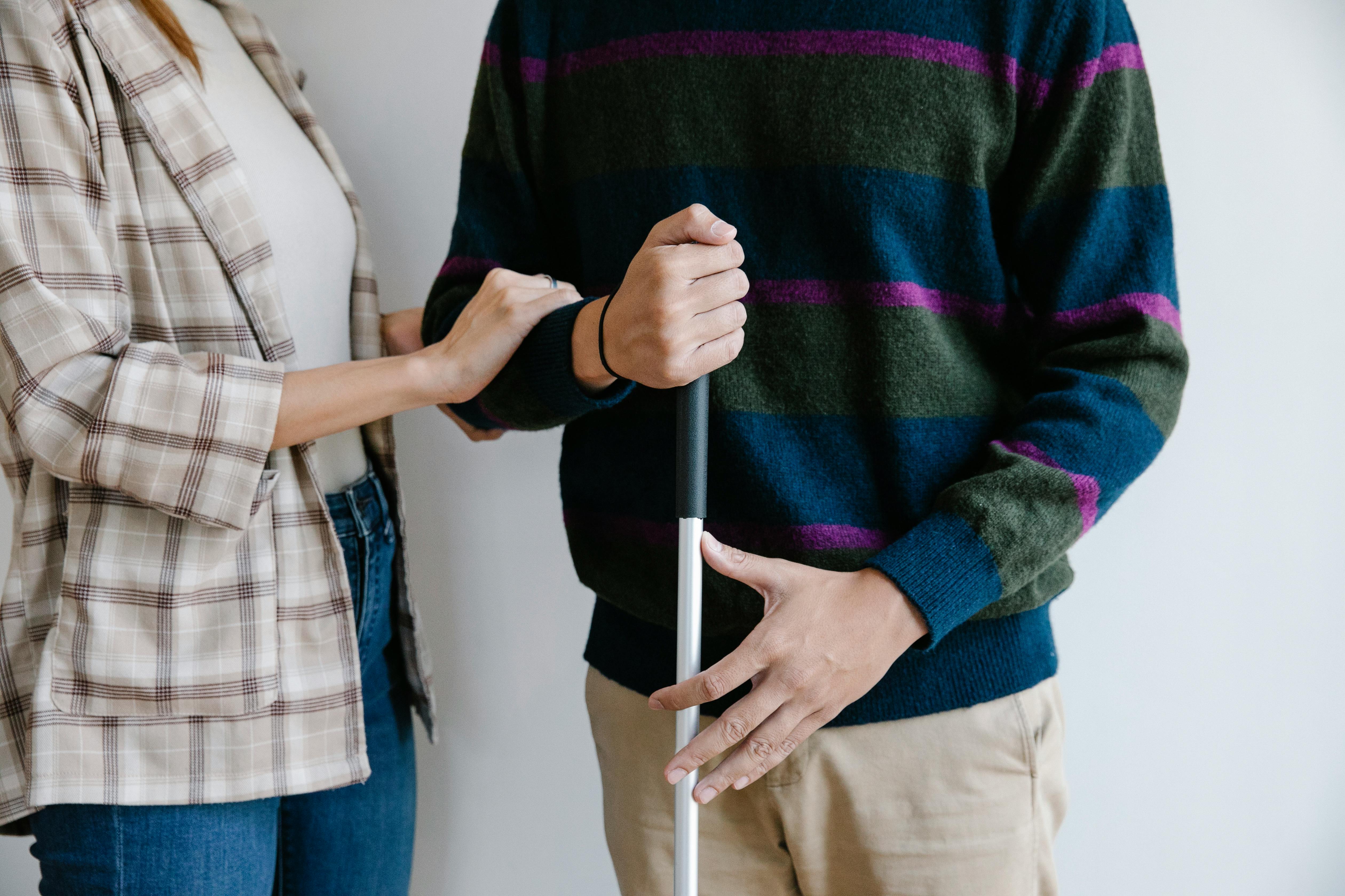 A professional walking alongside and supporting a man using a white cane