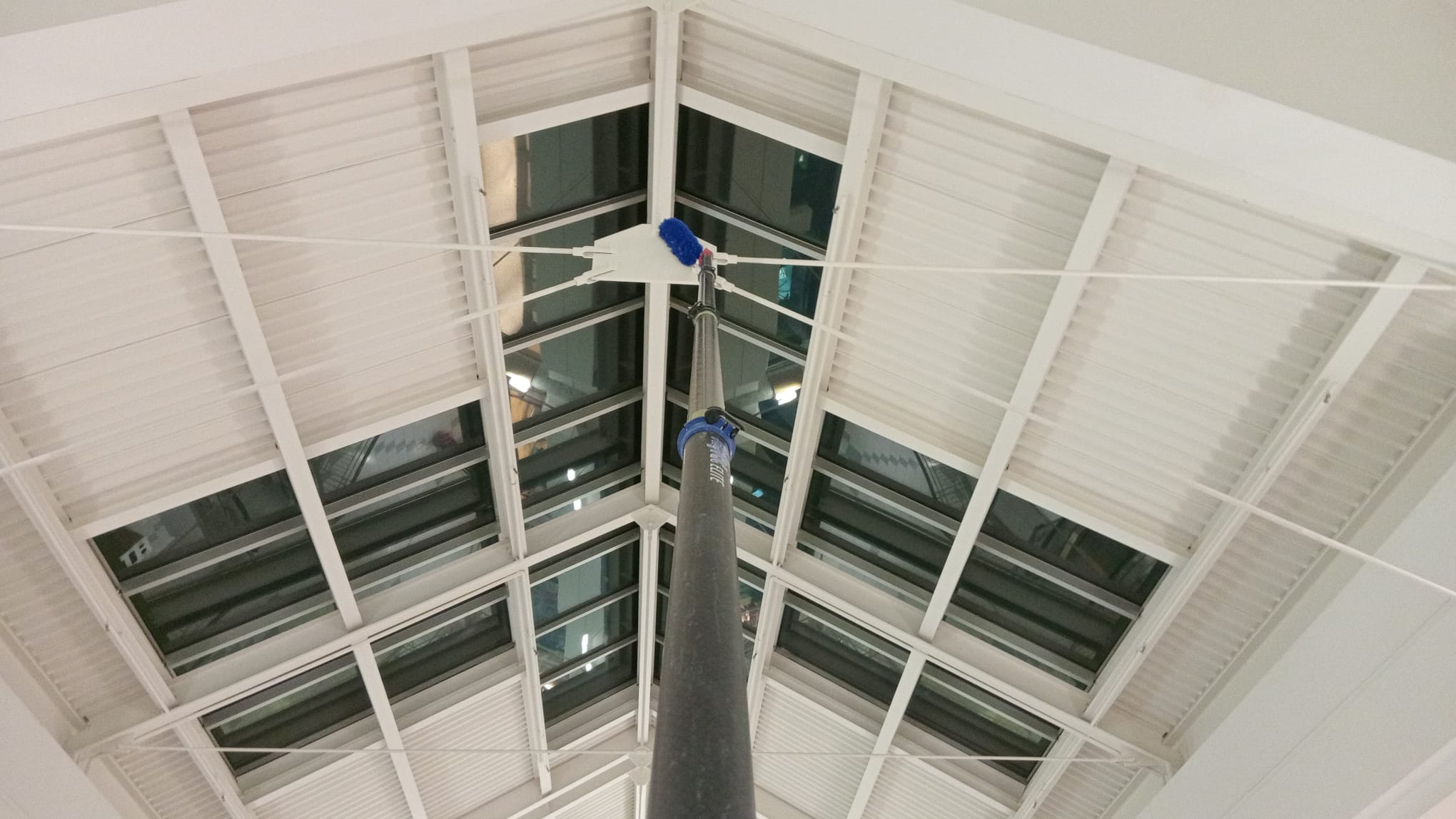 Extension pole with microfibre head cleaning the apex of a skylight truss in a shopping centre ceiling