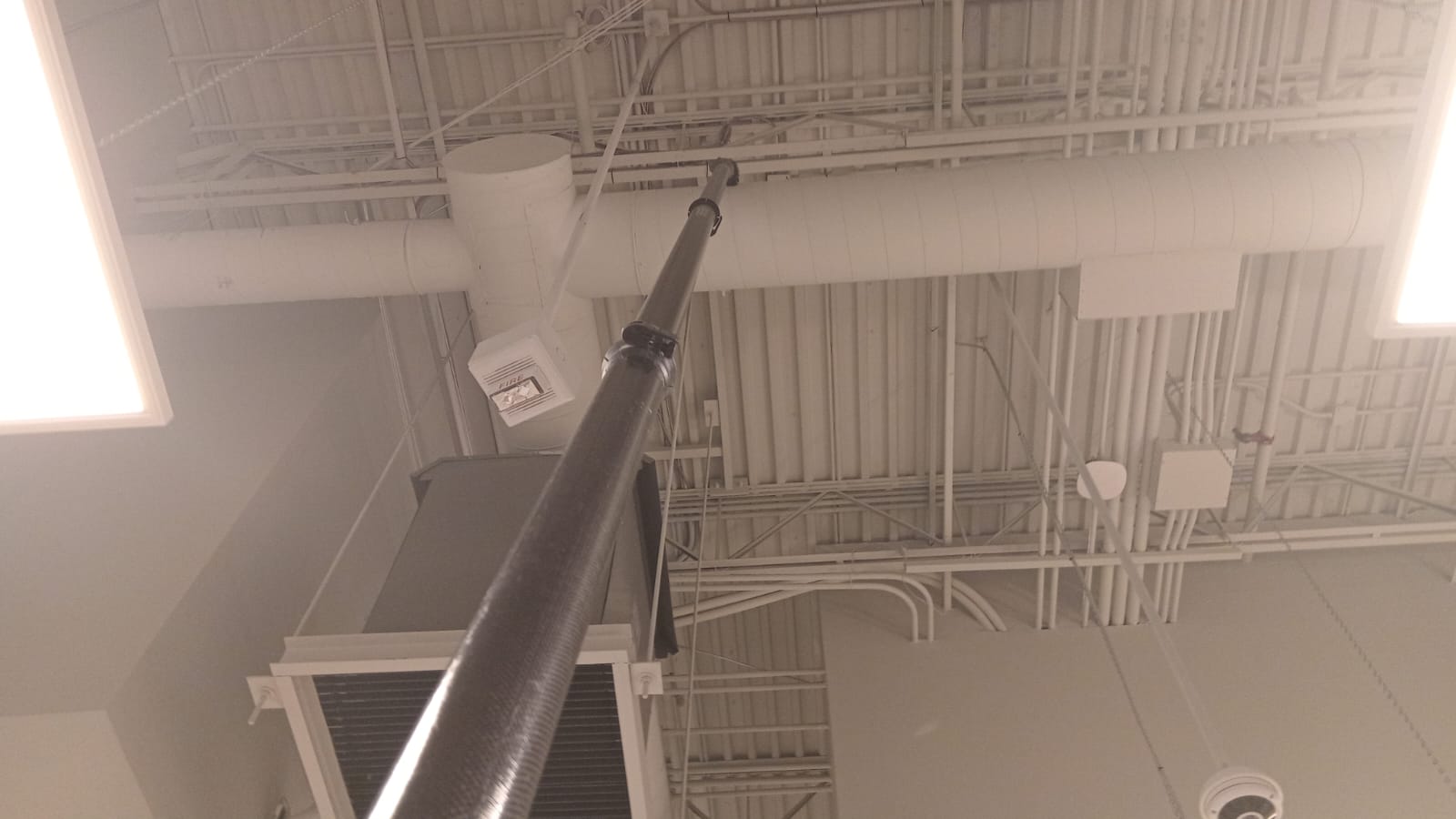 Extension pole cleaning an exposed ceiling deck with conduit and ductwork runs