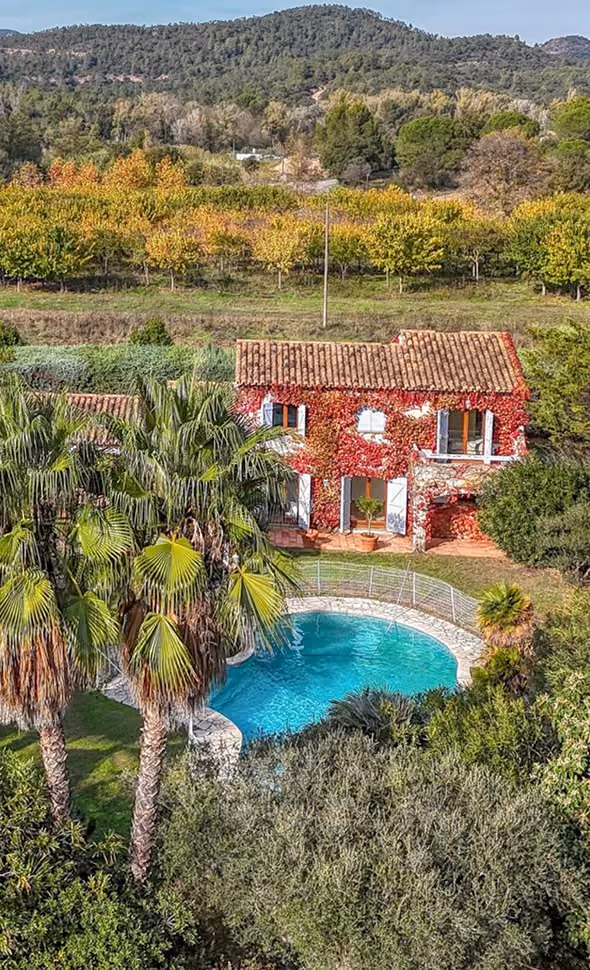 Vue aérienne d'un mas provençal en pierre rouge et de sa piscine entourés de vignes