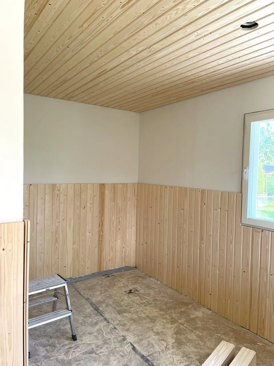 Remontoitavassa huoneessa on vaalea puupaneelikatto ja seinien alaosat, valkoiset yläseinät ja betonilattia.