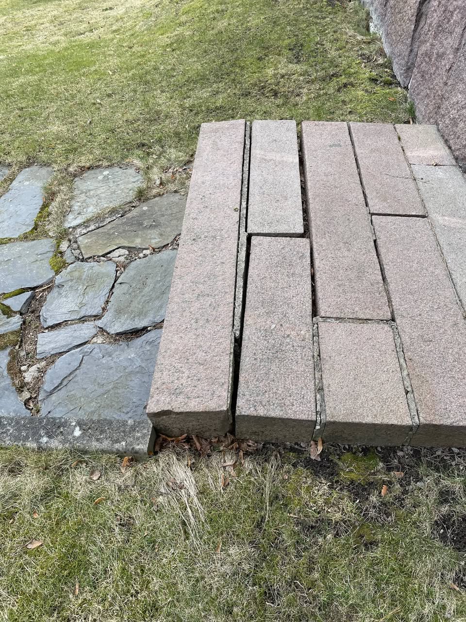Nurmikon ja liuskekivipolun vieressä on rivi suorakaiteen muotoisia graniittilaattoja.