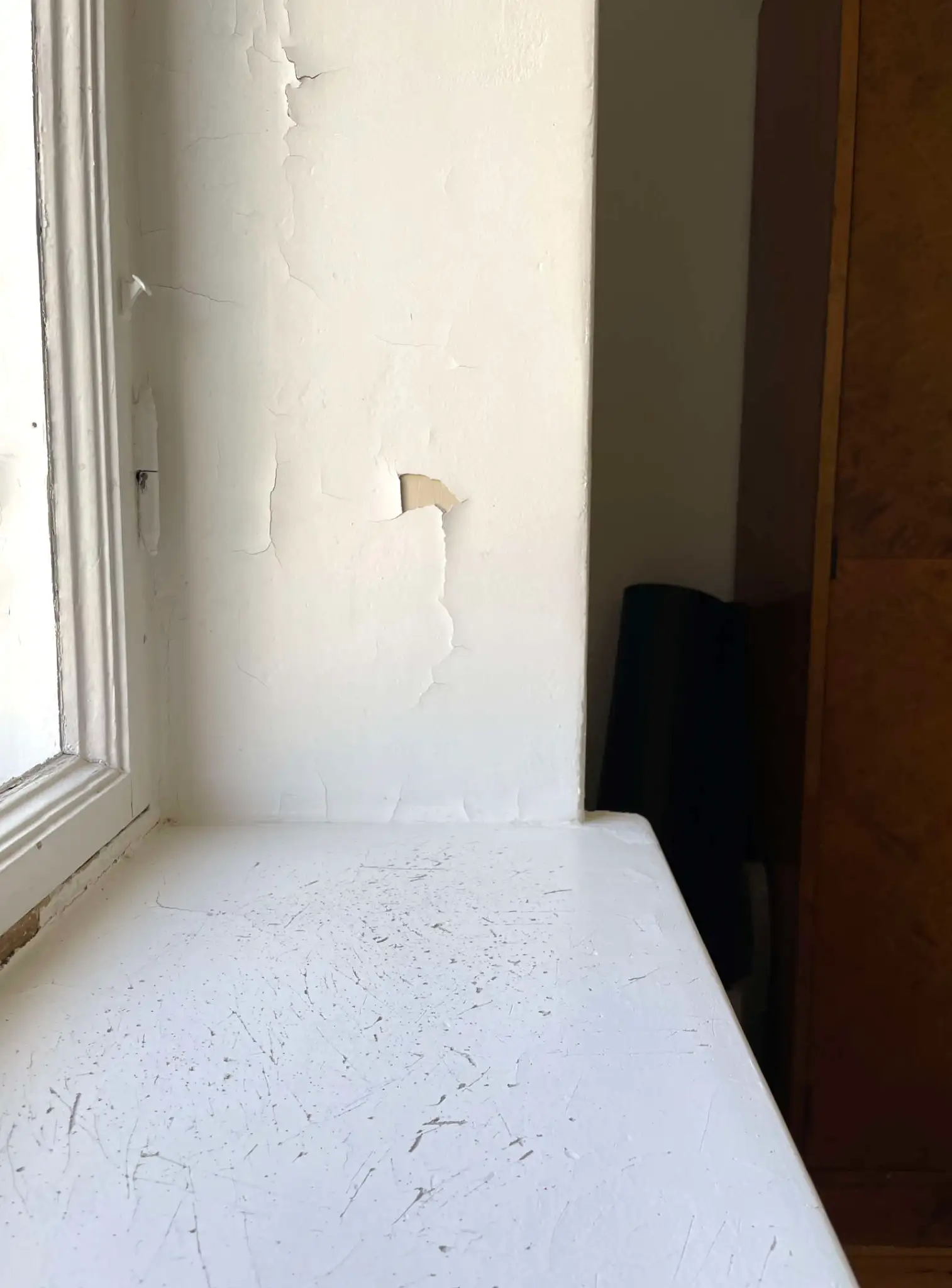 Seinän maalipinta hilseilee ja ikkunalauta on kulunut, mikä viittaa huoneistoremontin tarpeeseen.