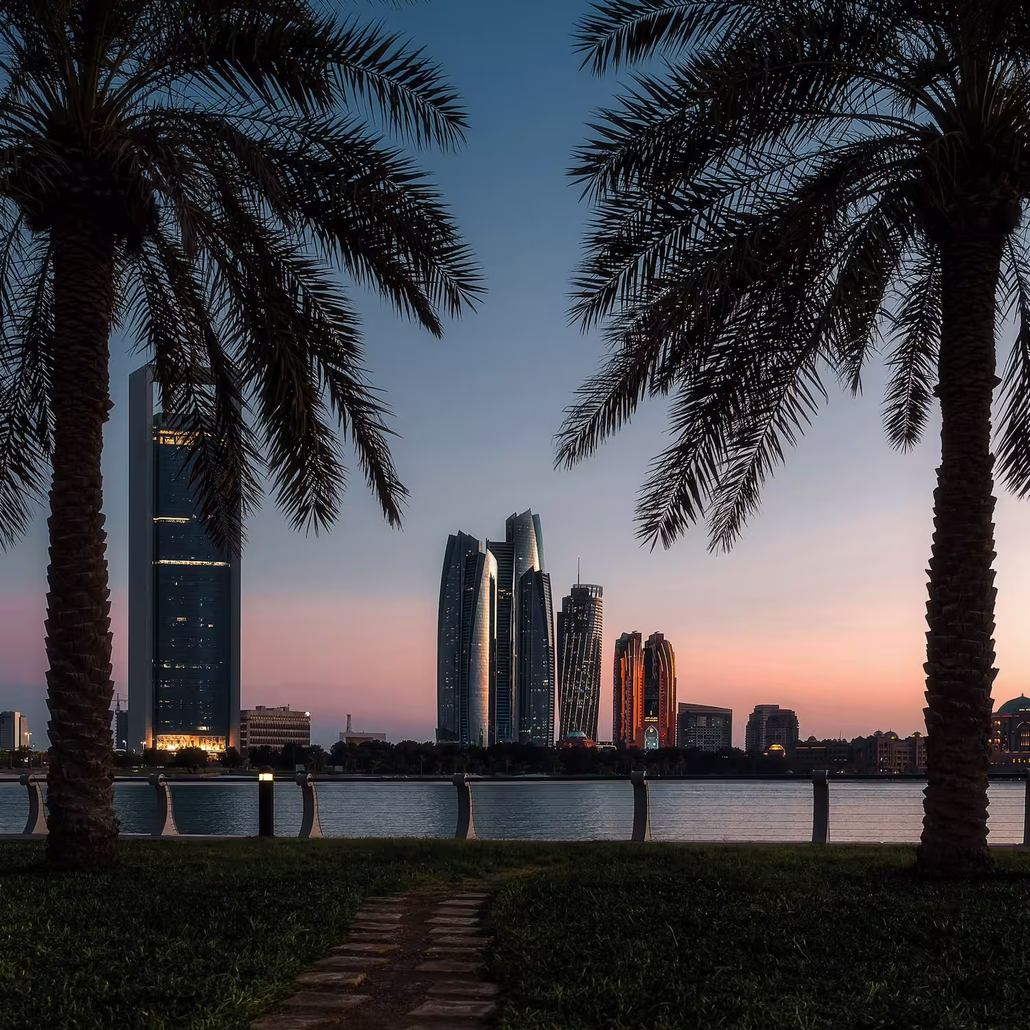 Abu Dhabi skyline at dusk viewed through palm trees