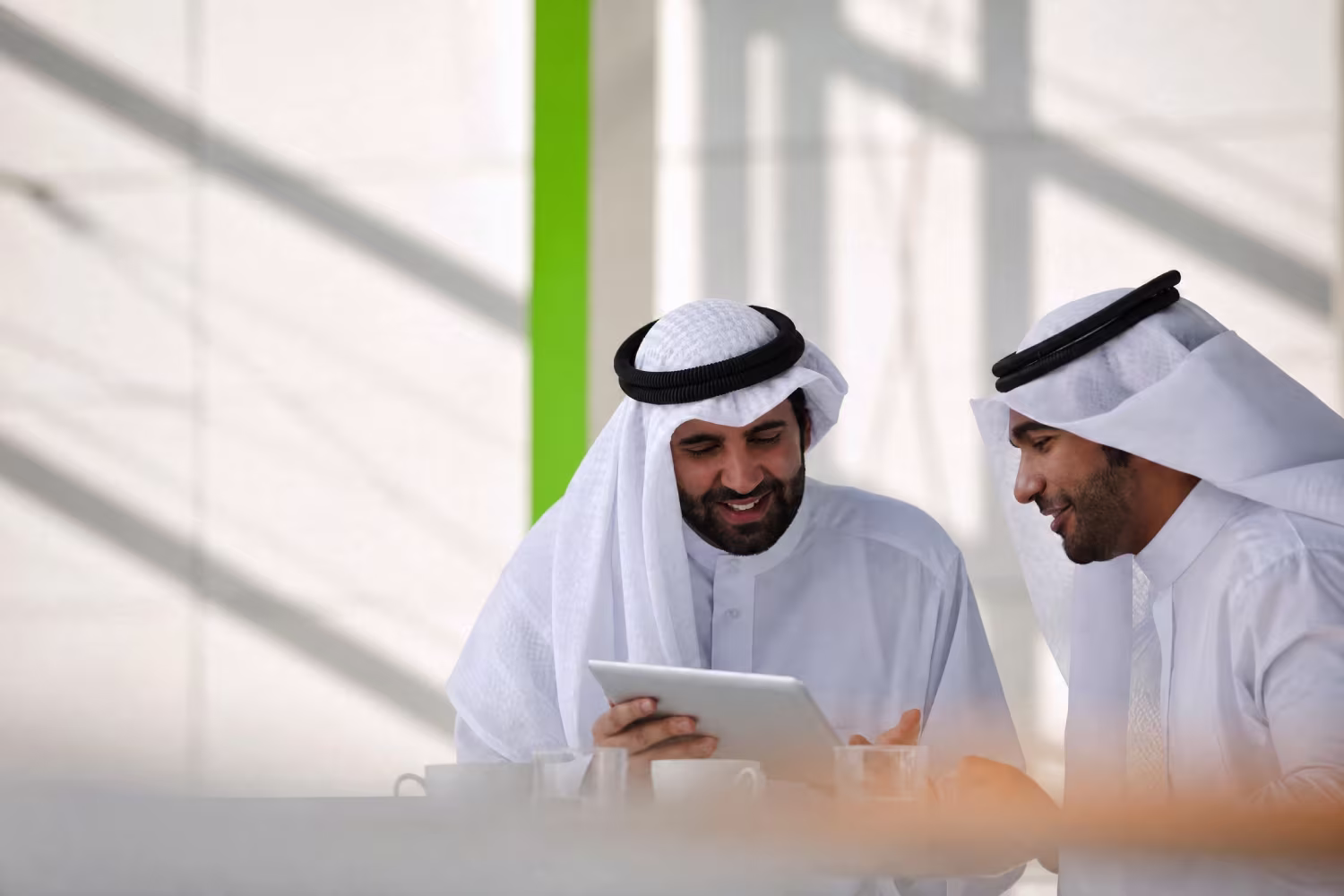 Two men in traditional Emirati dress reviewing a tablet together